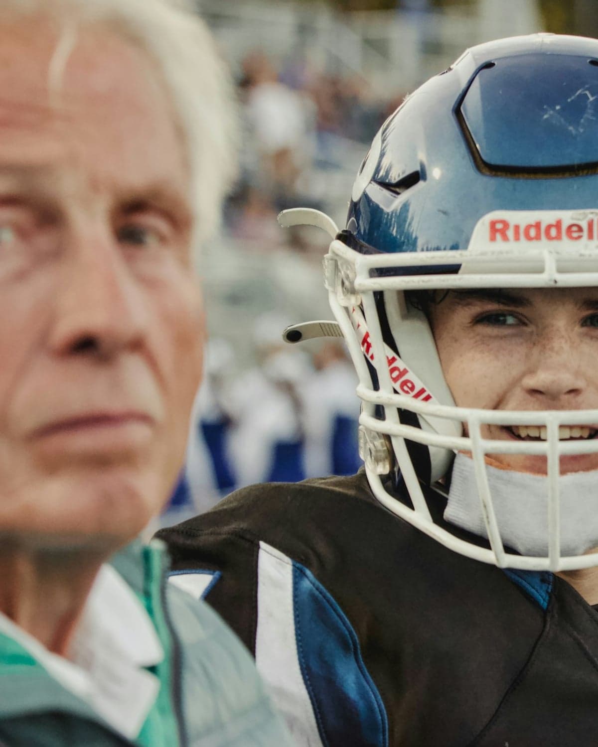 A high school football player in a helmet standing on the sideline beside a coach