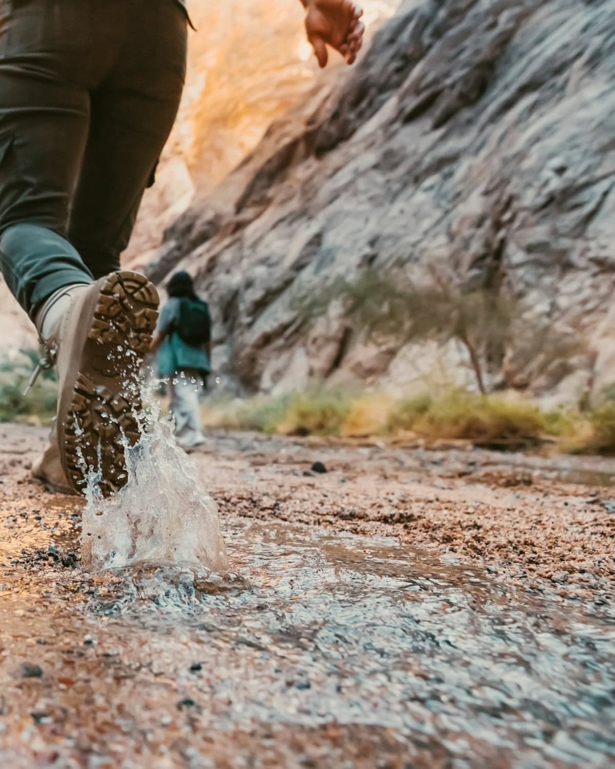 A hiker's boot splashing through shallow water on a rocky trail